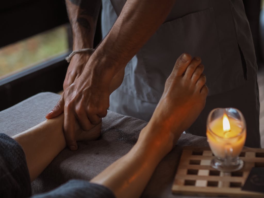 Close-up of a soothing foot massage in a dimly lit spa setting with a candle.